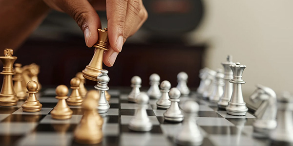 Close-up image of a hand picking up a chess piece at a chess table.